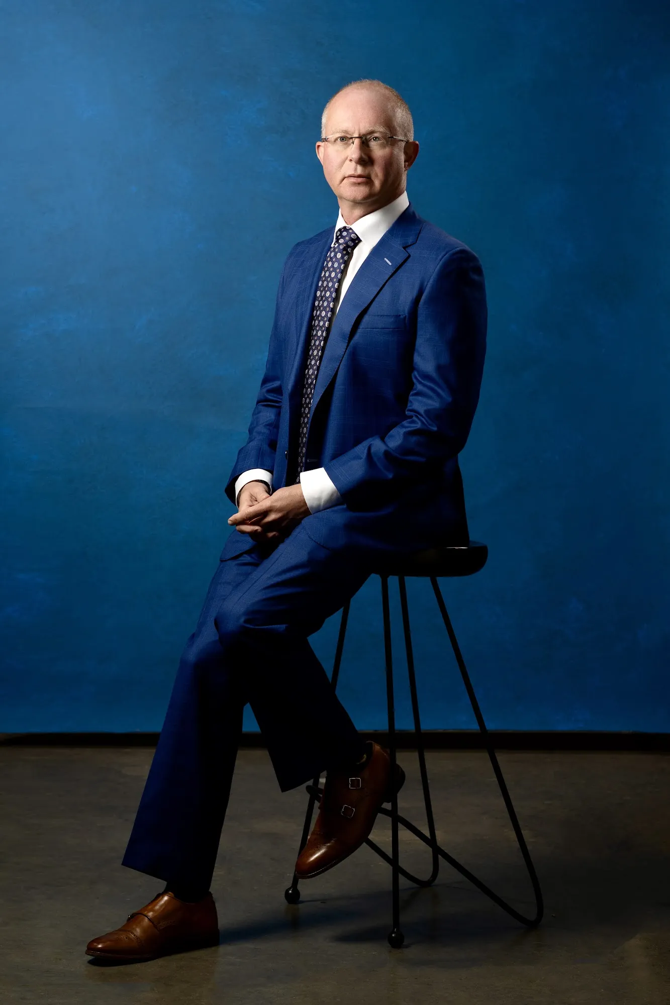 Executive in a blue suit seated on a stool against a blue backdrop