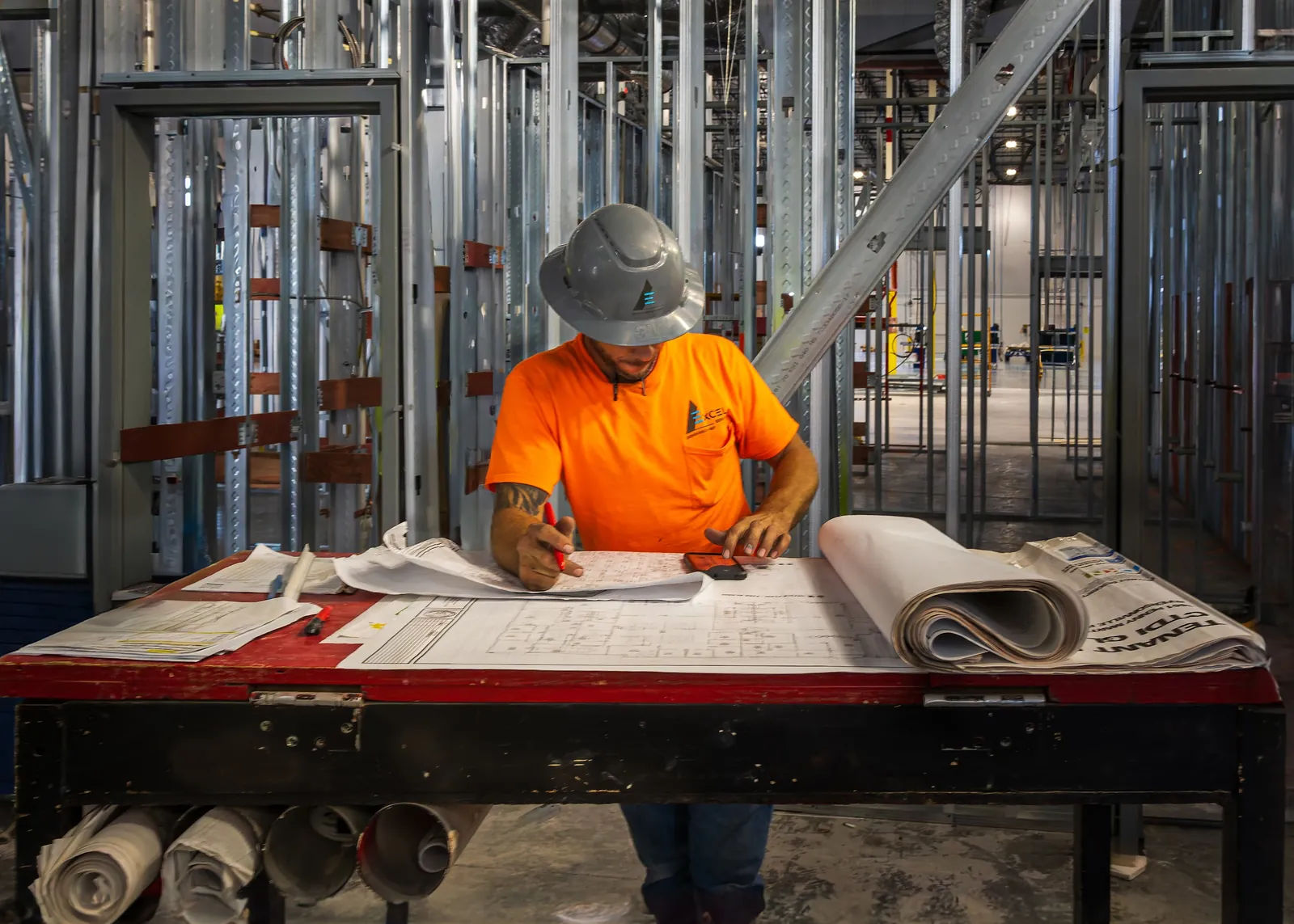 Worker in an orange shirt reviewing plans among steel framing