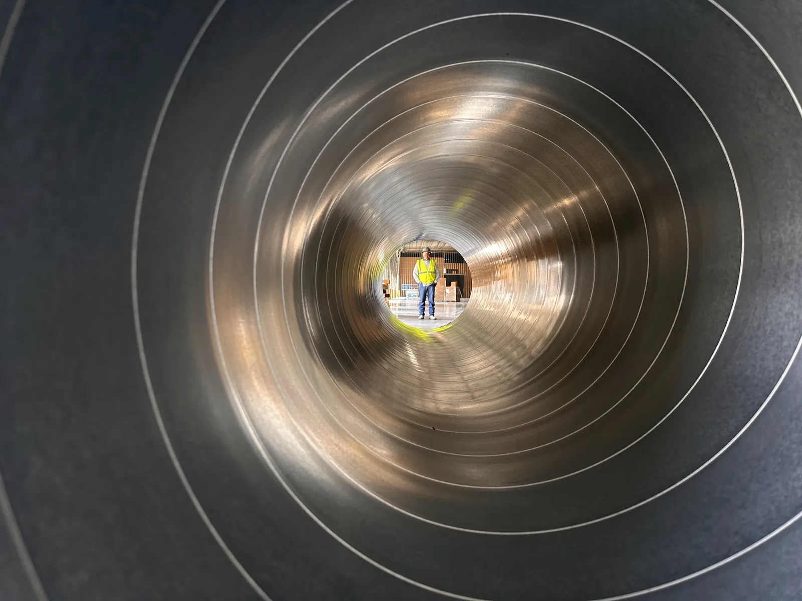 Looking through a large steel duct to a worker at the far end