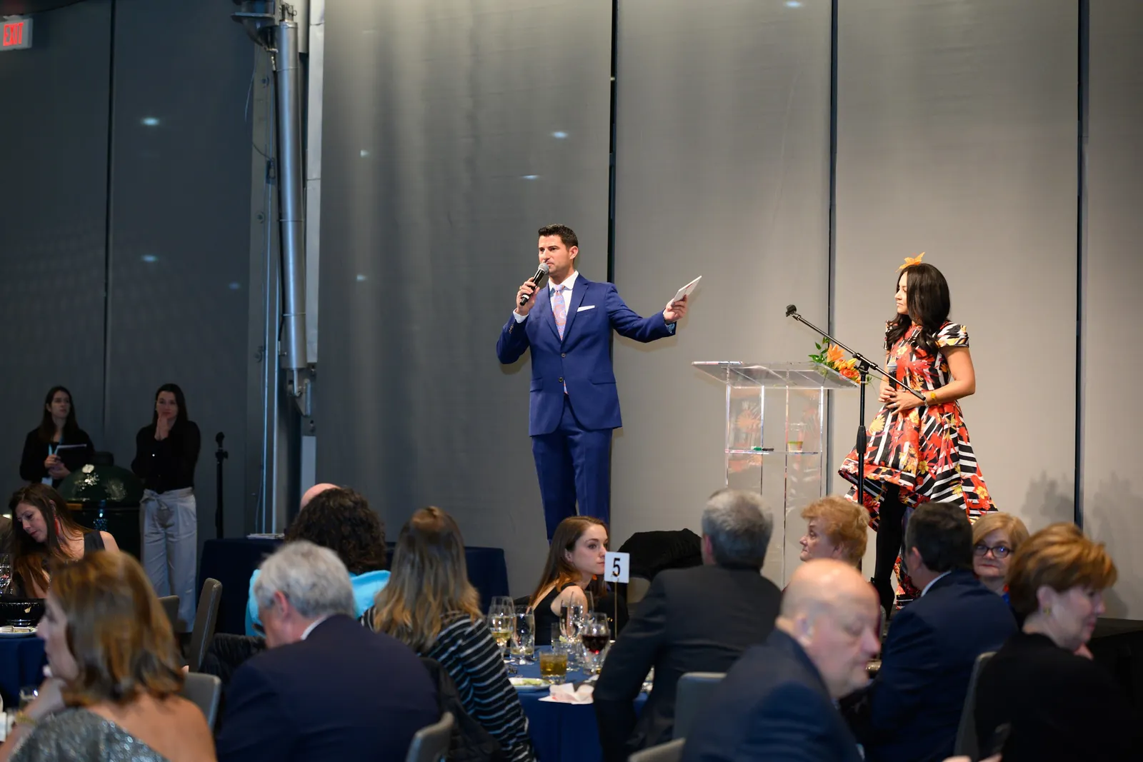 Speakers on stage presenting to a seated audience at a gala dinner