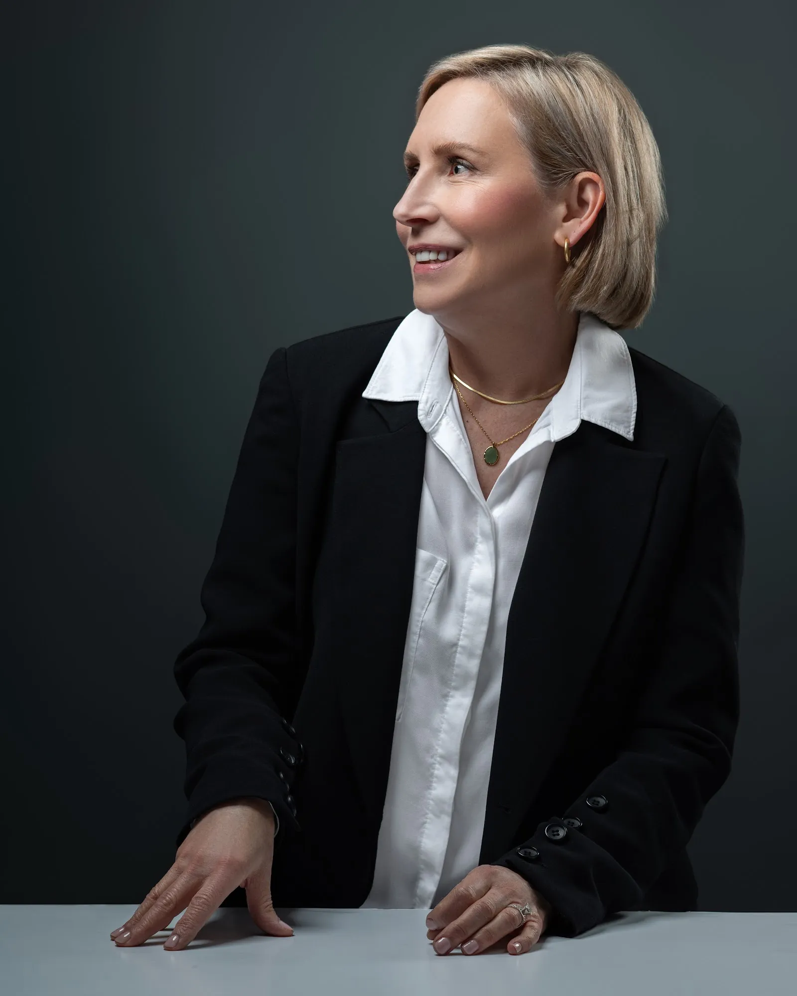 Executive in a black blazer looking toward window light, dark studio background