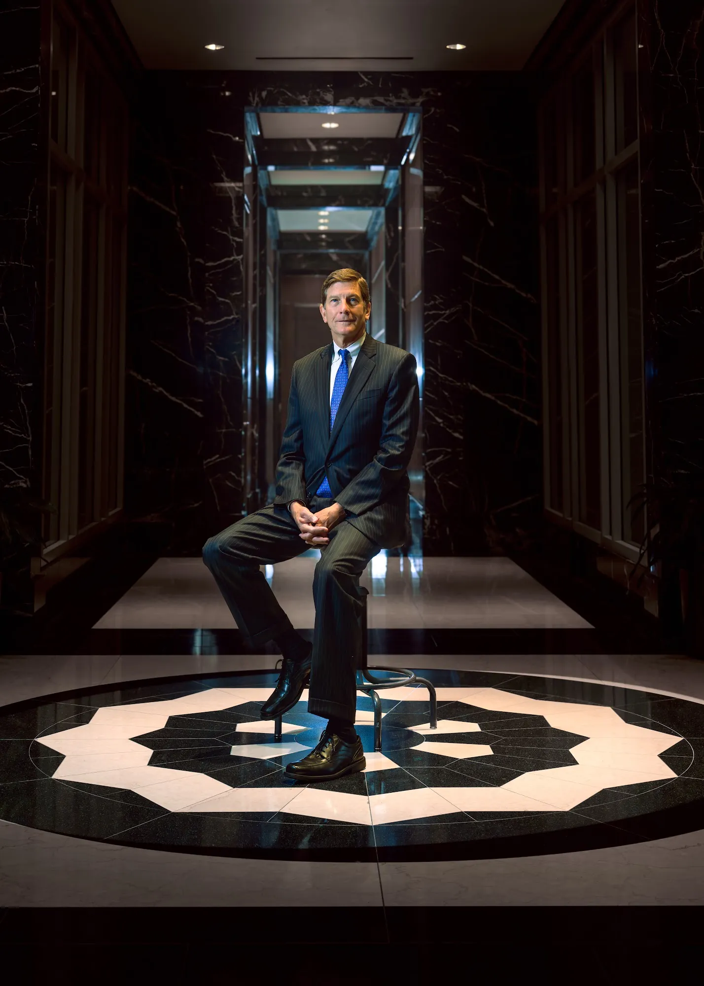 Executive seated on a stool in a dark marble lobby
